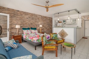 Ein Schlafzimmer mit Bett, Sofa, Sessel, einem kleinen Tisch, Deckenventilator und einer Küchenzeile.