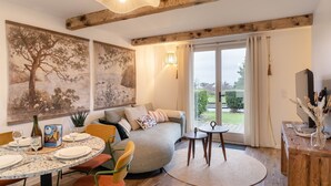 A cozy living room with a round dining table, a sofa, and a large window with curtains. - La Croisée des Sentiers - Aperçu Vue Mer (Pléneuf-Val-André)