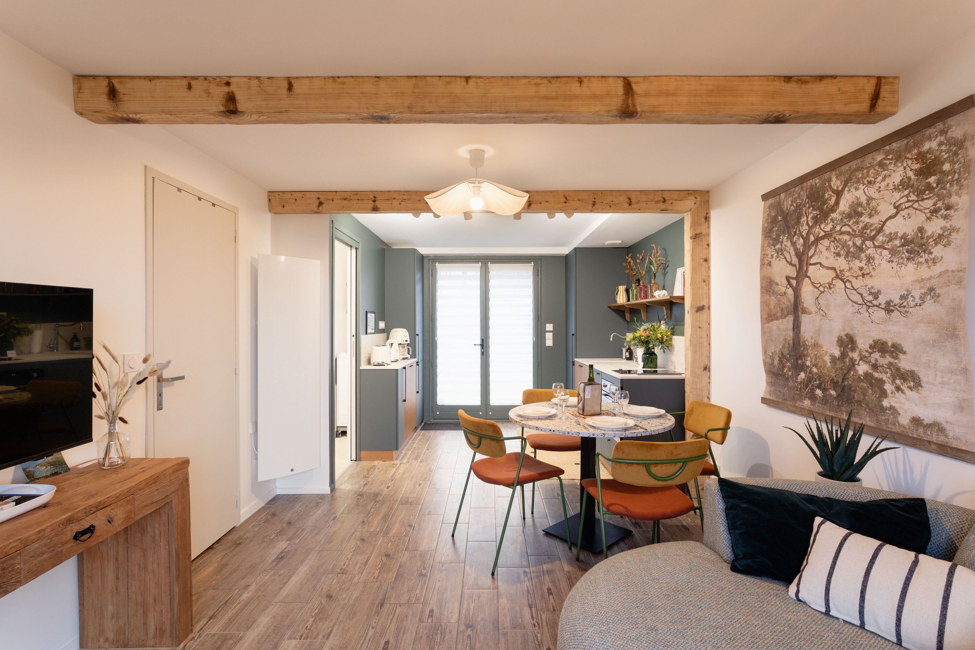 A modern living room with a wooden ceiling, a dining area with orange chairs, and a large painting on the wall.