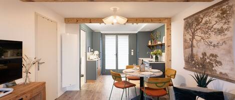 A modern living room with a wooden ceiling, a dining area with orange chairs, and a large painting on the wall.