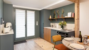 A modern kitchen with a dining area, featuring a wooden beam ceiling, a built-in oven, and a dining table set for two. - La Croisée des Sentiers - Aperçu Vue Mer (Pléneuf-Val-André)