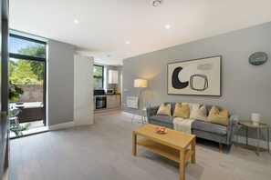 A modern living room with a grey sofa, a wooden coffee table, and a large abstract artwork on the wall. - 4BR w/ Jacuzzi, Garden & Parking (London)