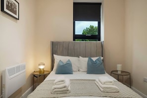 A hotel room with a bed, a window with a view, a bedside table with a lamp, and a radiator. - 4BR w/ Jacuzzi, Garden & Parking (London)
