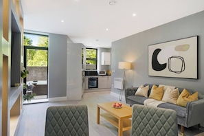 A modern living room with a grey sofa, a coffee table, and a dining area with a table and chairs. - 4BR w/ Jacuzzi, Garden & Parking (London)