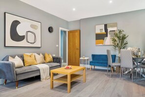 A modern living room with a grey sofa, a wooden coffee table, and a blue sofa. - 4BR w/ Jacuzzi, Garden & Parking (London)