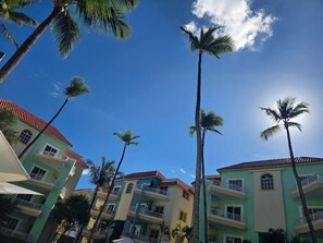 A multi-story hotel with balconies, palm trees, and a clear blue sky. - Beautiful 2-bedrooms tropical condo, 1-st floor, few minutes from the beach (Punta Cana)