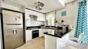 A modern kitchen with white cabinets, a stainless steel refrigerator, a black countertop, and a small dining area with white chairs. - Luxury villa with Jacuzzi and BBQ 150 meters from the beach (Punta Cana)