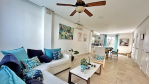 A modern living room with a white sofa, teal cushions, a coffee table, and a ceiling fan. - Luxury villa with Jacuzzi and BBQ 150 meters from the beach (Punta Cana)