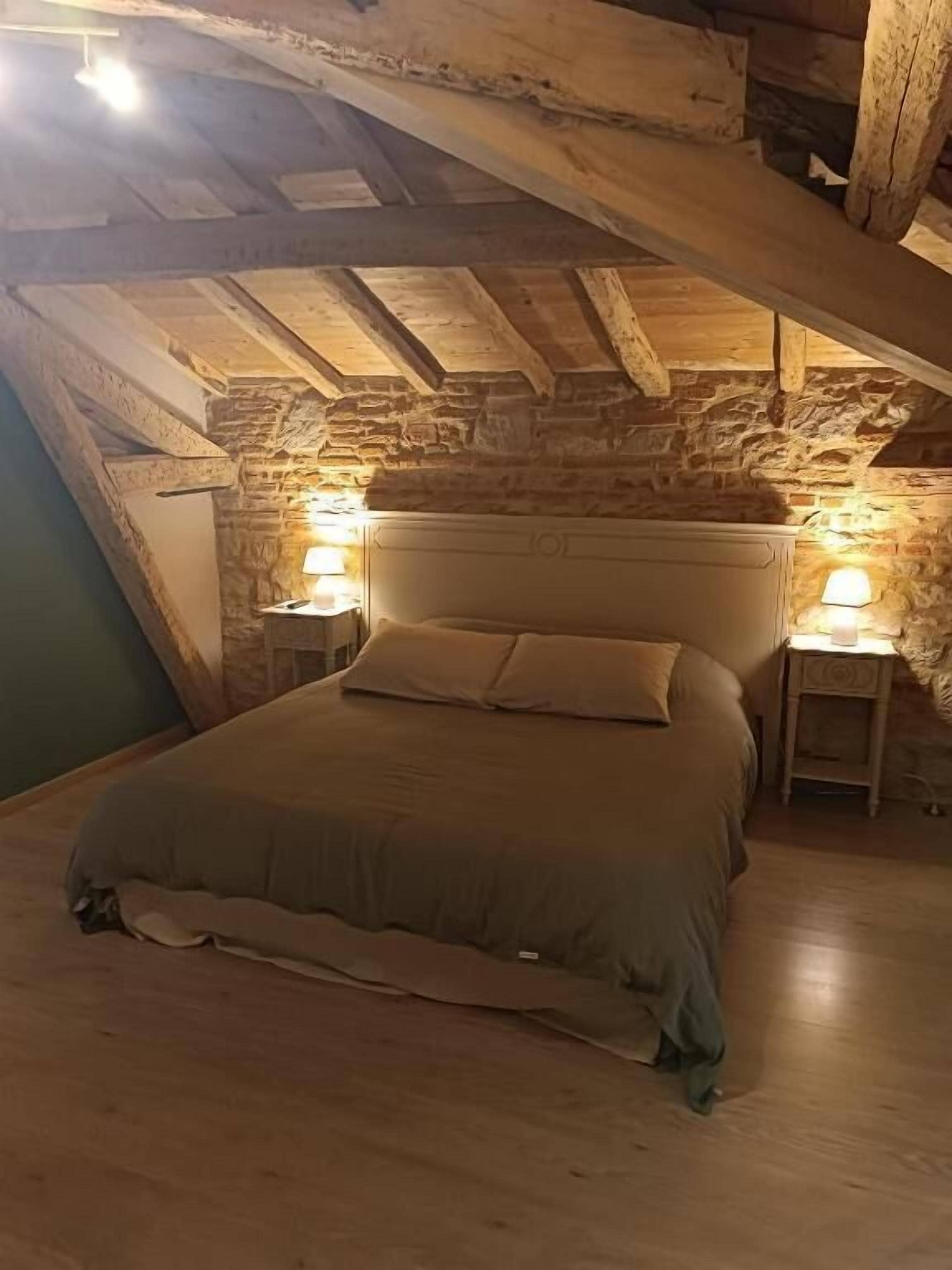 Un dormitorio acogedor en un ático con pared de piedra, techo de madera y una cama con dos mesitas de noche.