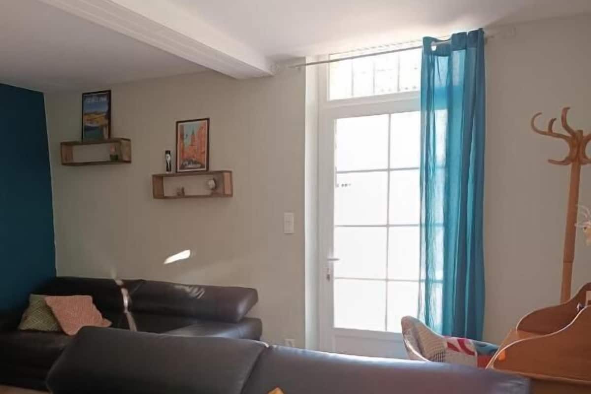 Ein Wohnzimmer mit einem schwarzen Ledersofa, einem hölzernen Kleiderständer und einem großen Fenster mit blauen Vorhängen.