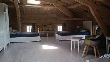 A loft-style room with exposed wooden beams, two beds, a small table, and a white cabinet.