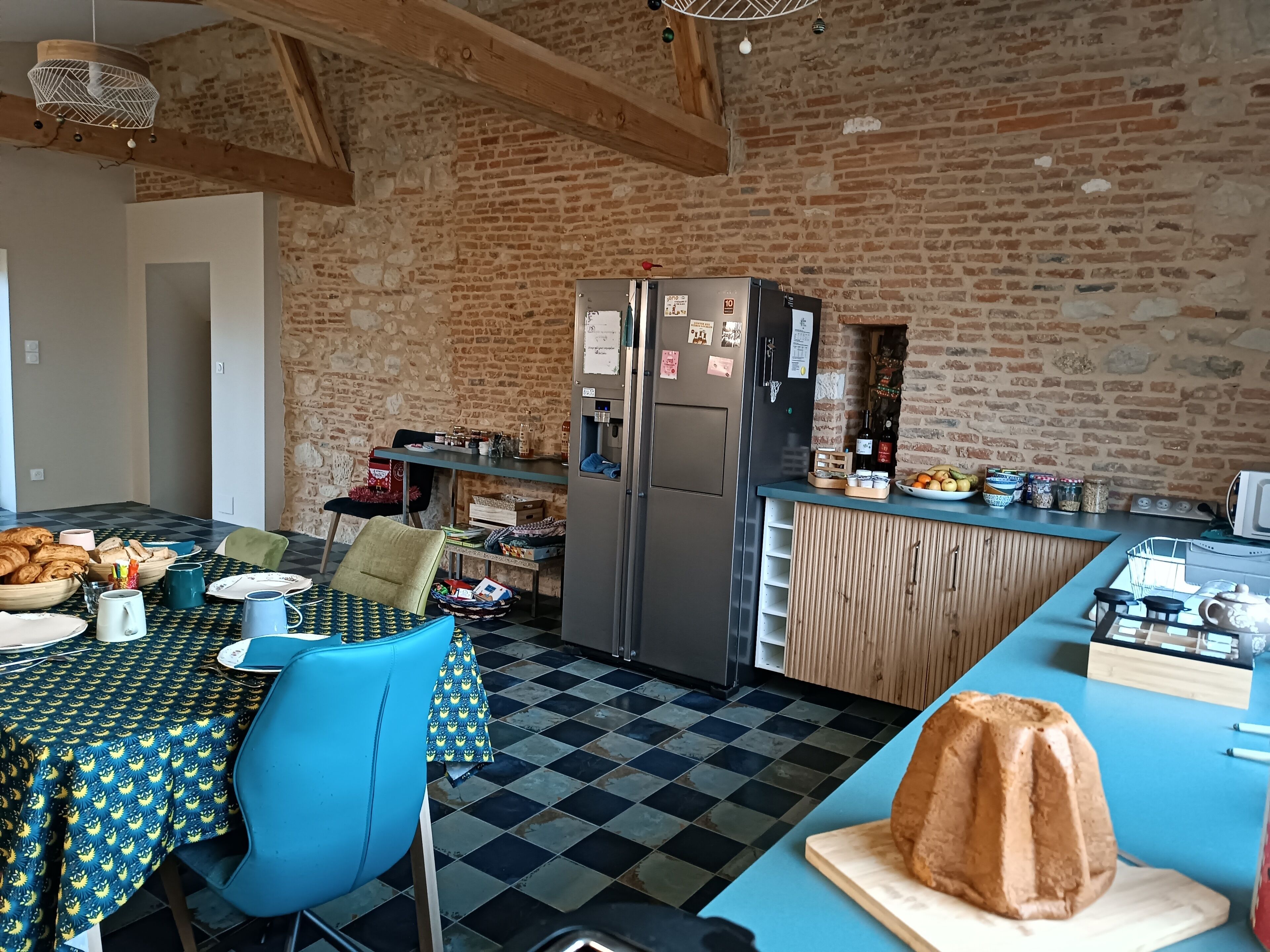 A rustic kitchen with a brick wall, a wooden ceiling, and a checkered floor.