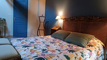 Un dormitorio con colcha estampada de flores, una puerta azul, una mesita de noche con lámpara y un cabecero de ratán.