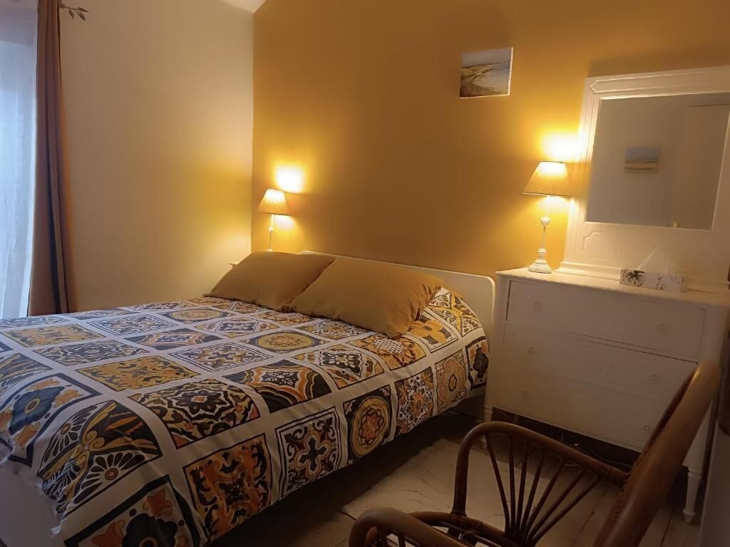 Une chambre à coucher avec une couvre-lit à motifs, des lampes de chevet, une petite table de chevet et une chaise.