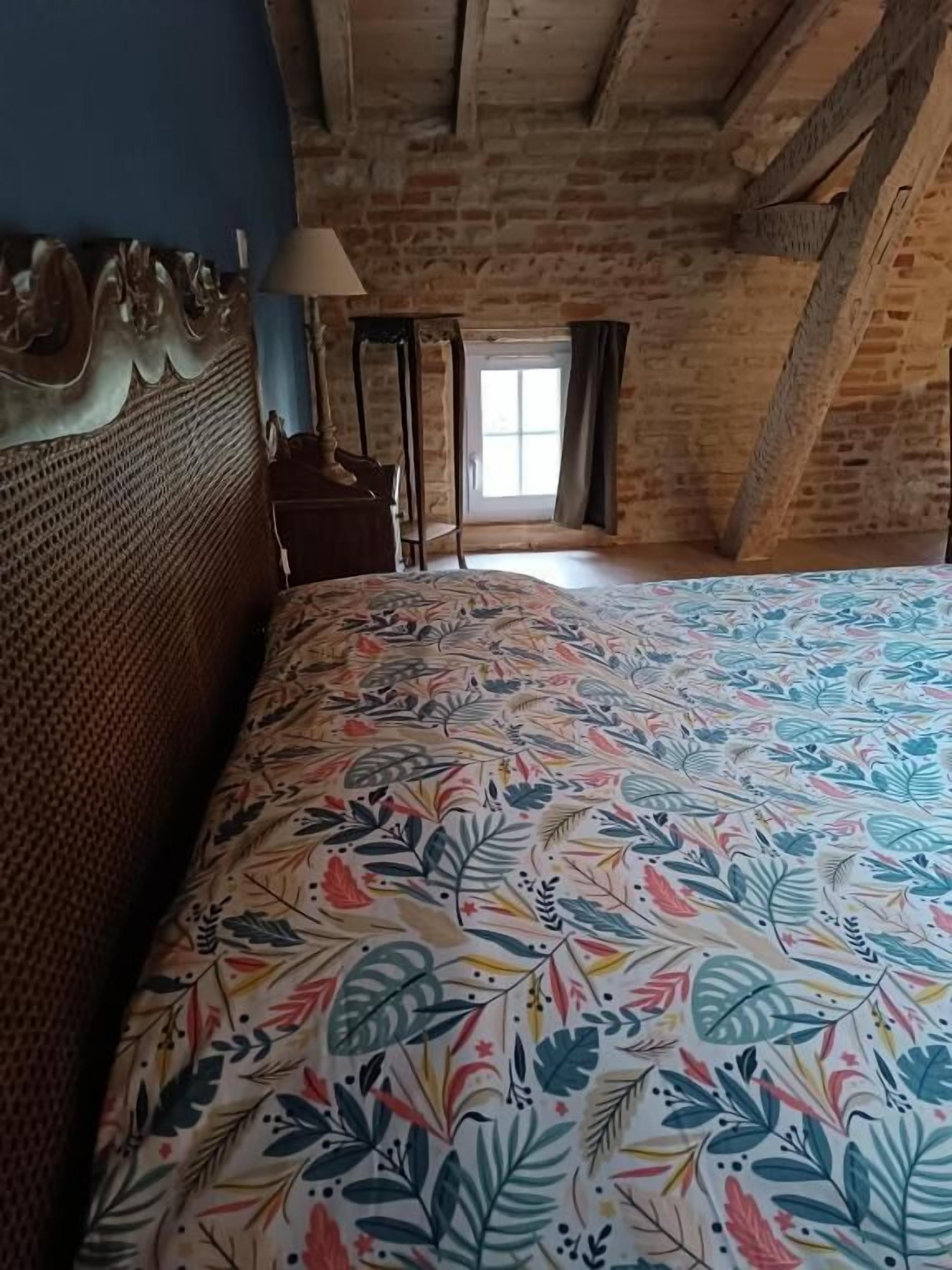 Una habitación con cama, cabecera de madera, ventana con cortinas y una lámpara.