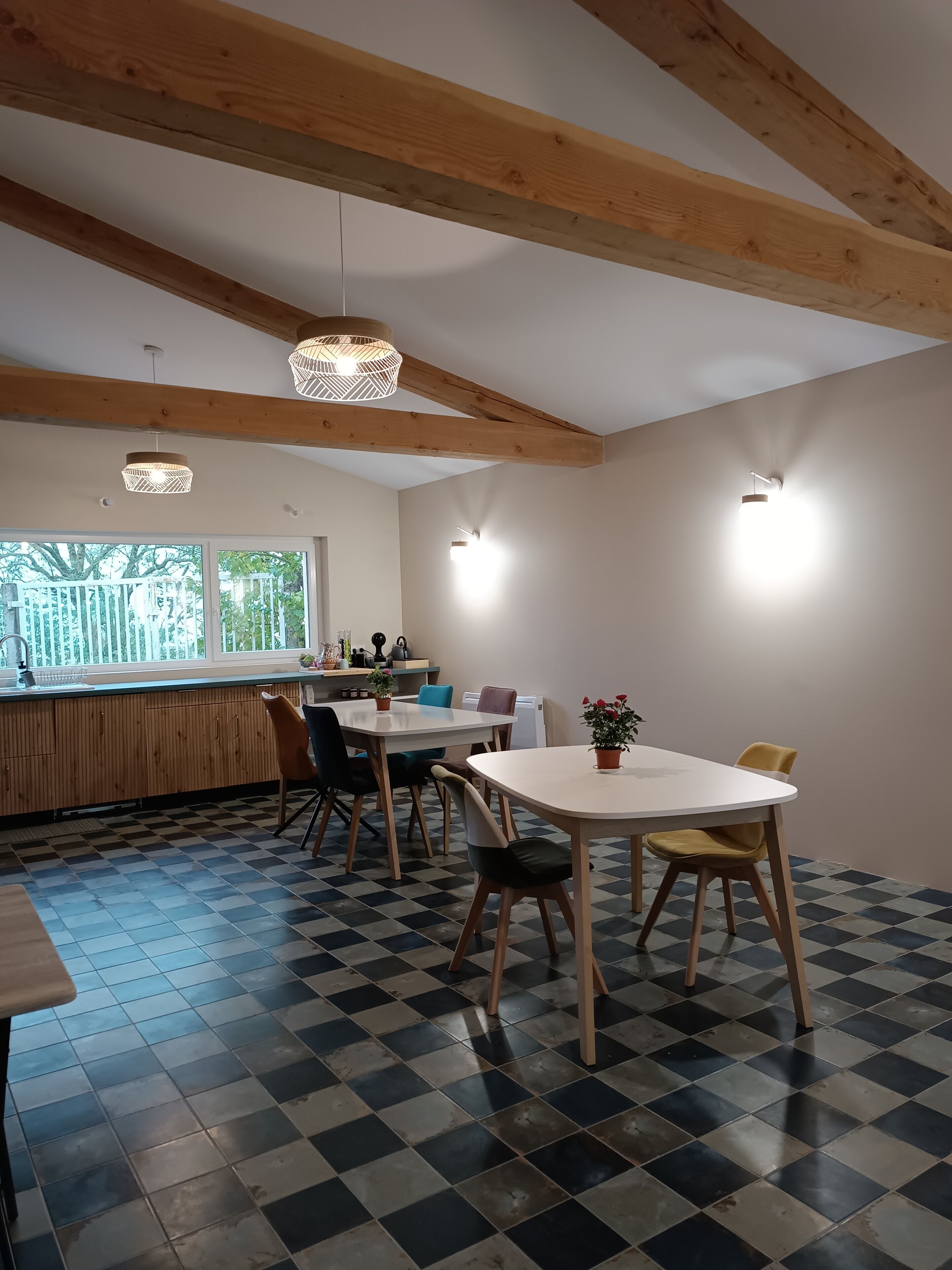 A modern kitchen with wooden beams, checkered floor tiles, and pendant lighting.