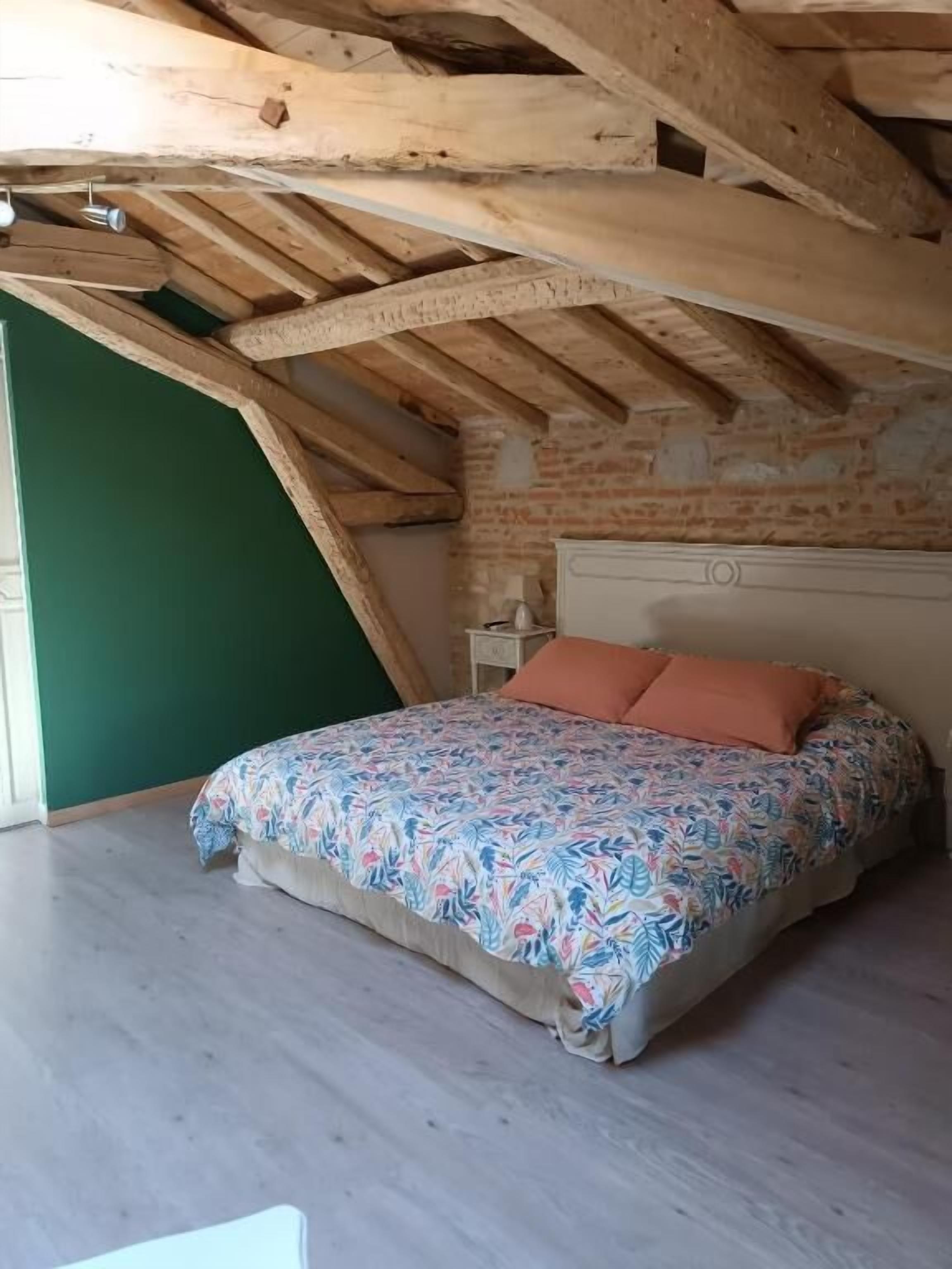 Un dormitorio con techo inclinado, una cama con colcha estampada y una pared de ladrillo.