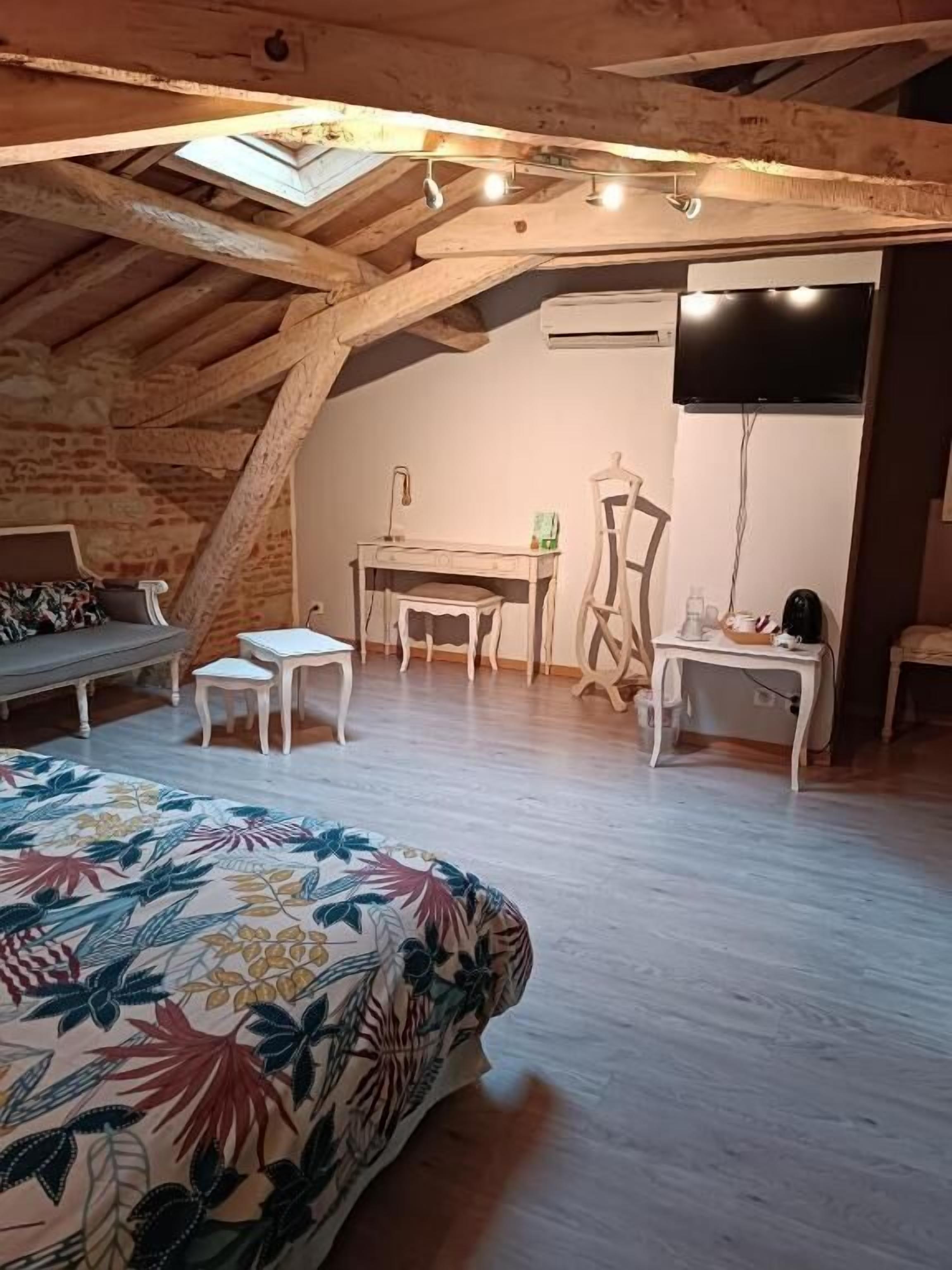 A cozy attic bedroom with a sloped ceiling, a bed with a floral bedspread, a desk, a chair, and a TV mounted on the wall.