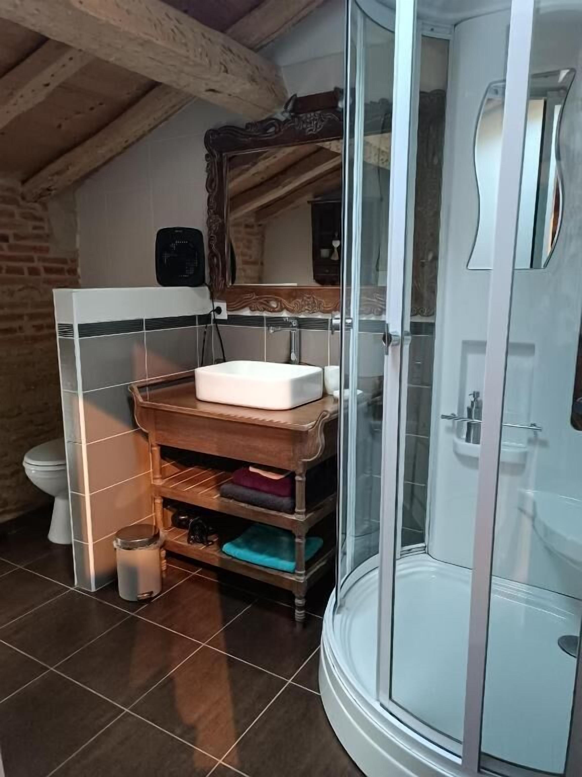 A bathroom with a glass shower enclosure, a wooden vanity with a mirror, and a tiled floor.
