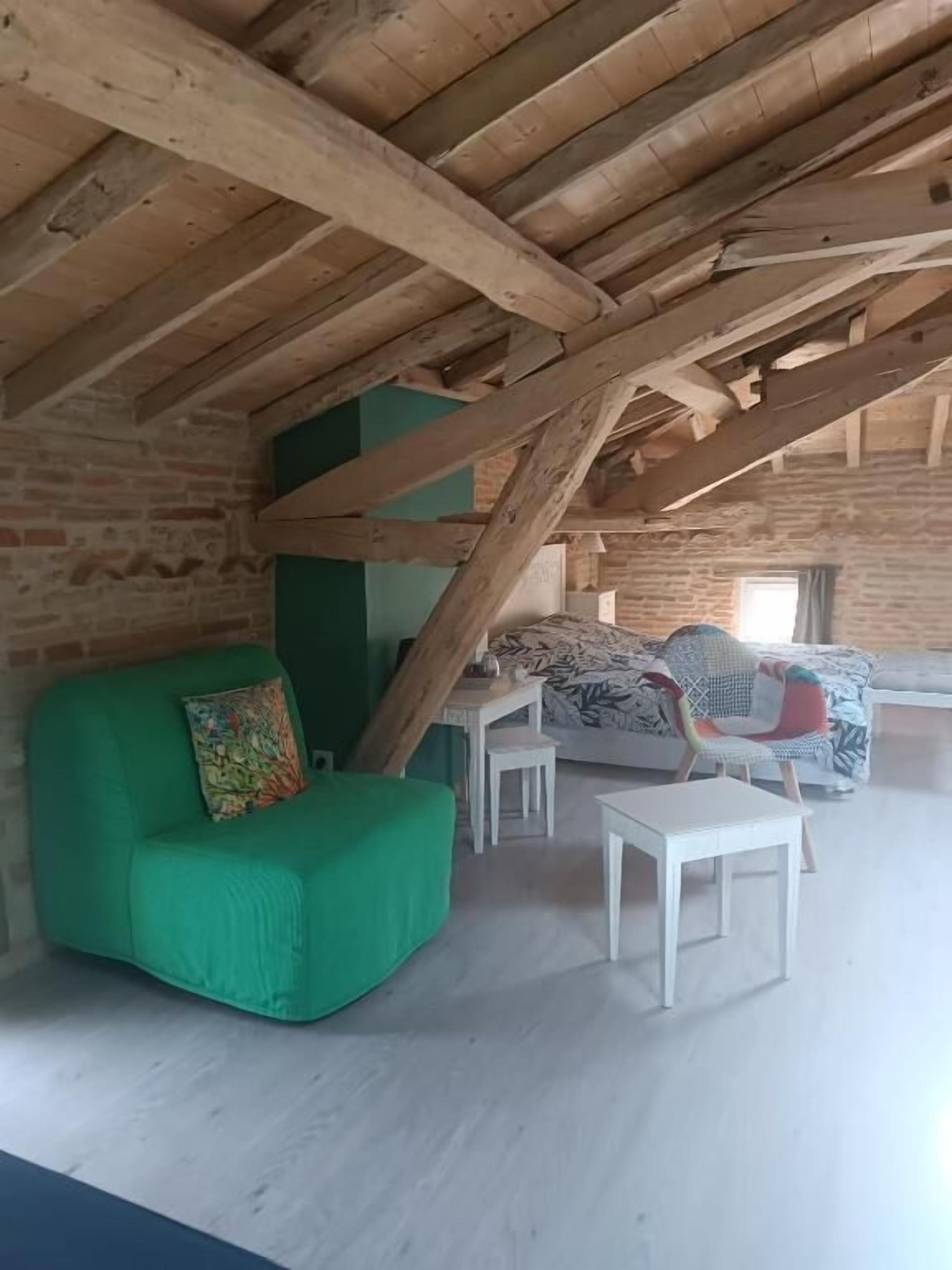 Una habitación rústica con vigas de madera a la vista, un sofá verde, un sillón estampado y una pequeña mesa blanca.
