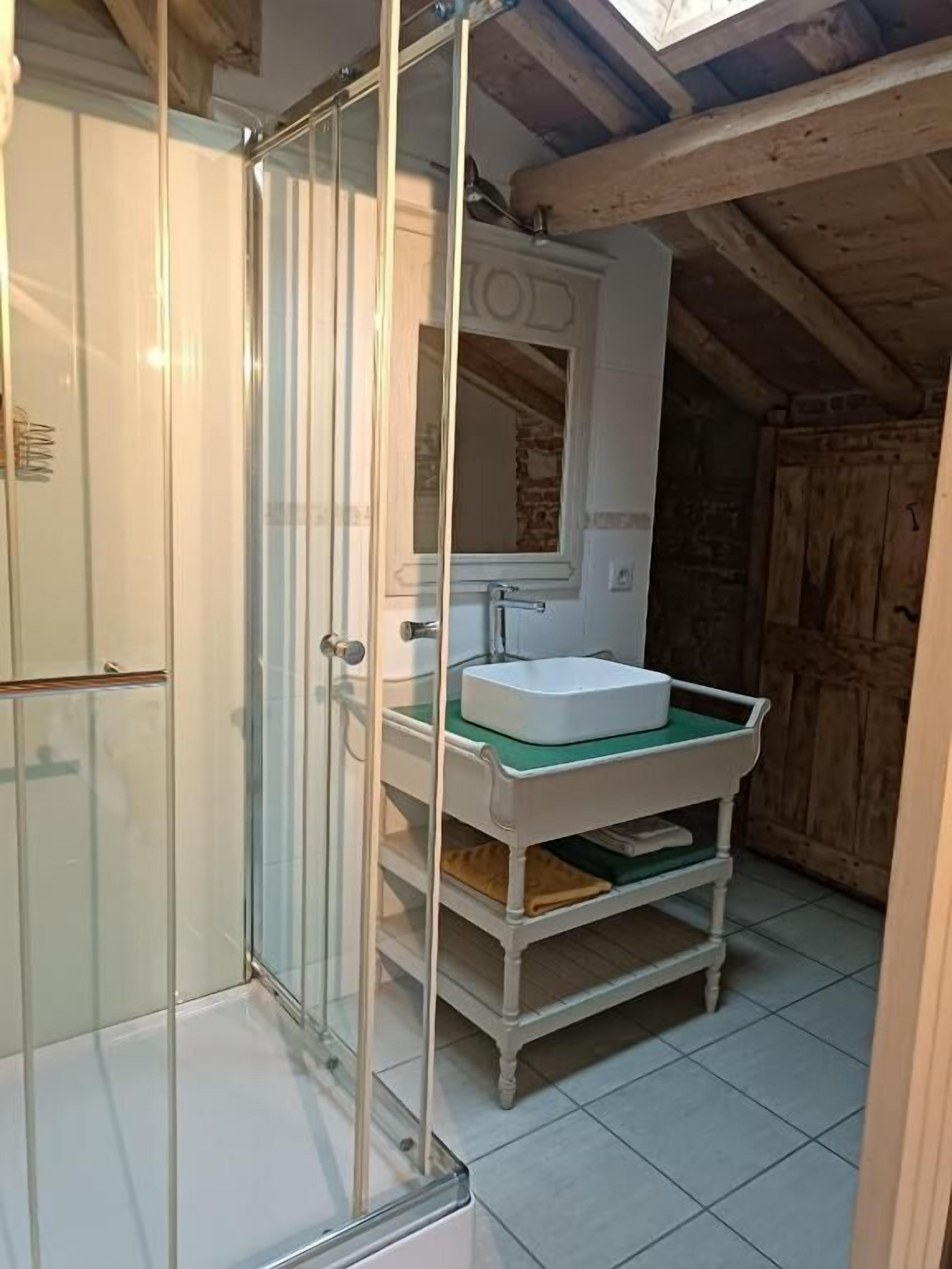 A bathroom with a glass shower enclosure, a white sink with a green mat, and a wooden ceiling.