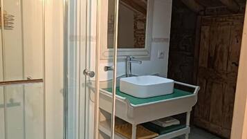 A bathroom with a glass shower enclosure, a white sink with a green mat, and a wooden ceiling.