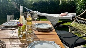 An outdoor dining area with a wooden table set for two, a hammock, and a chair. - Deichkoje12 - Deck 1 vacation apartment directly on the dike with dog | North Sea near (Tönning)