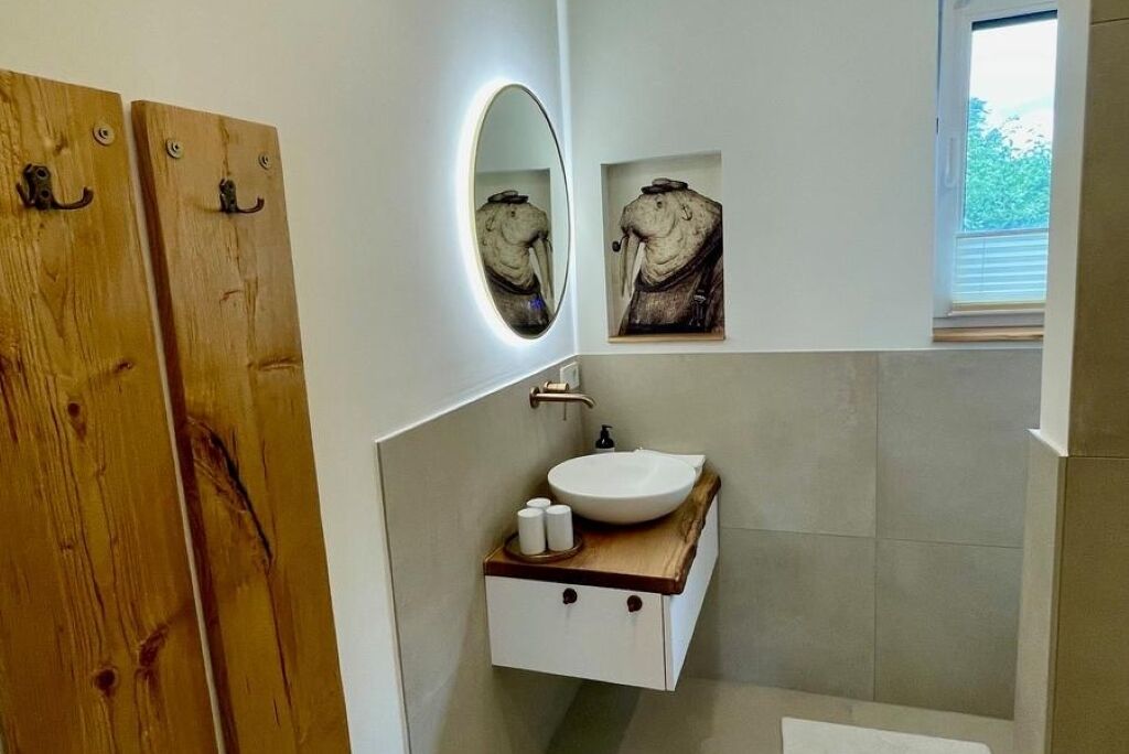 A bathroom with a wooden door, a white sink with a wooden countertop, a mirror, and a framed artwork above the mirror.