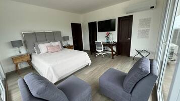 Ett modernt hotellrum med en stor säng, två grå fåtöljer, ett skrivbord med en stol, en TV och ett fönster med utsikt.