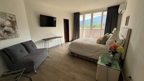 A modern hotel room with a bed, a sofa, a small table, and a TV mounted on the wall. - Luxury 3BR Penthouse City Mall SPS (San Pedro Sula)
