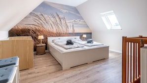 Ein Schlafzimmer mit schrägem Dach, einem Bett mit Kissen, einem Nachttisch, einer Lampe und Blick zum Himmel durch ein Fenster.