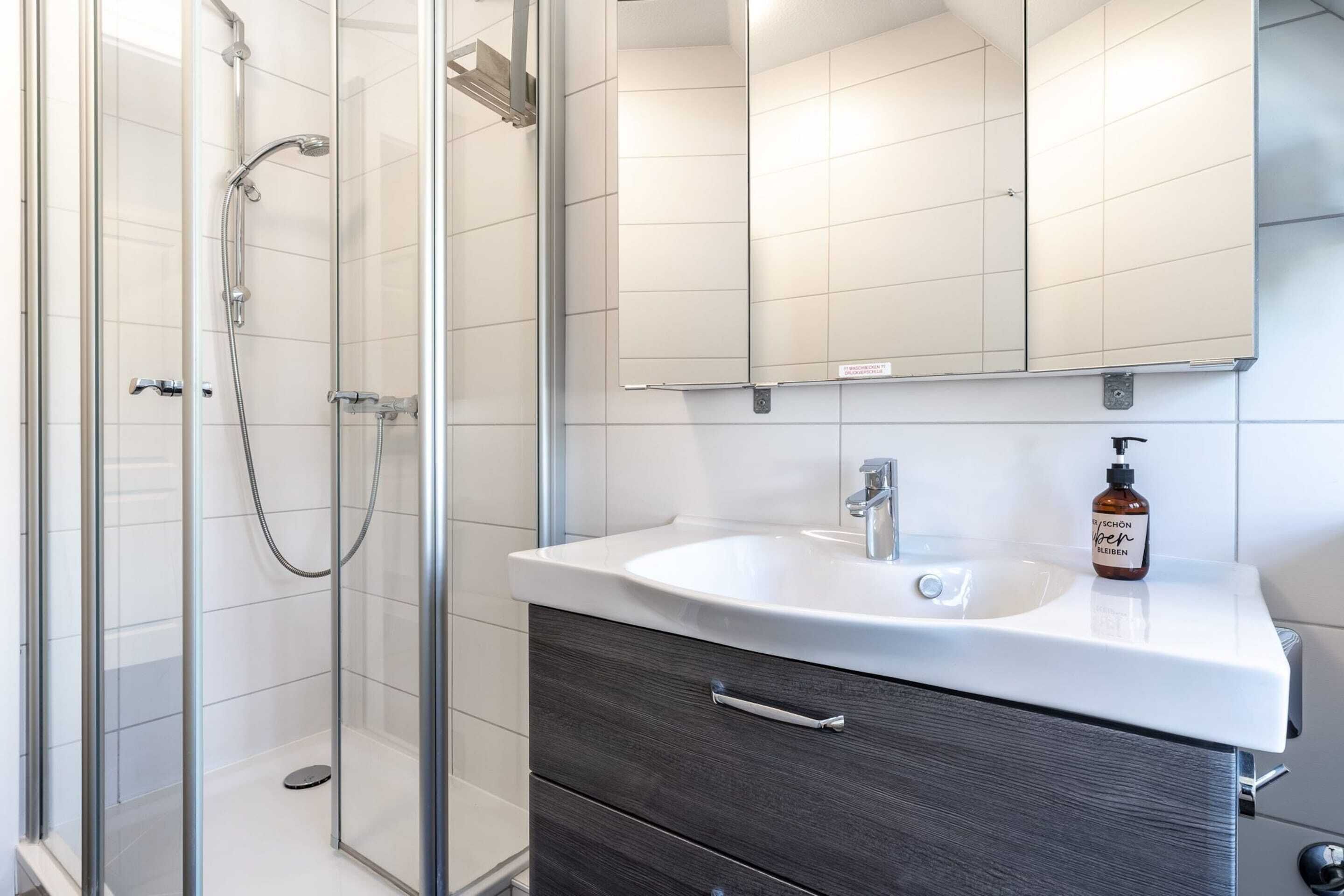 Un baño moderno con cabina de ducha acristalada, un lavabo blanco con mueble oscuro y un espejo grande sobre el lavabo.