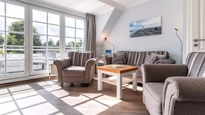 Ein modernes Wohnzimmer mit einem großen Fenster, einem Sofa, zwei Sesseln, einem Couchtisch und einem Gemälde an der Wand.