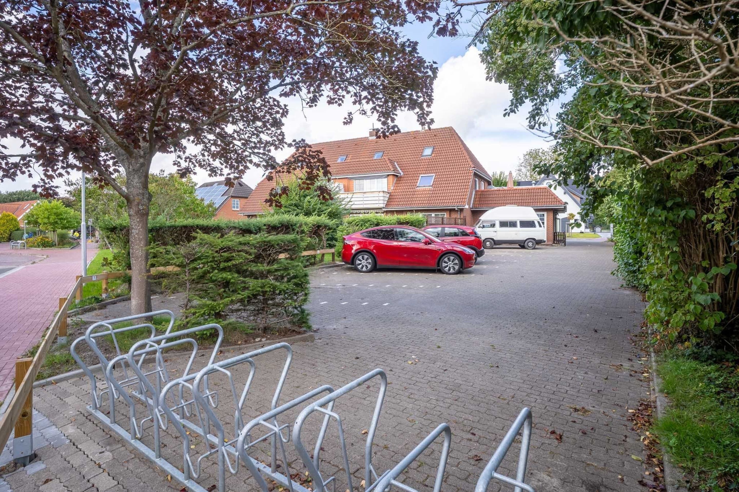 A residential street with a red car parked on the side, a white van, and a house with a red roof.
