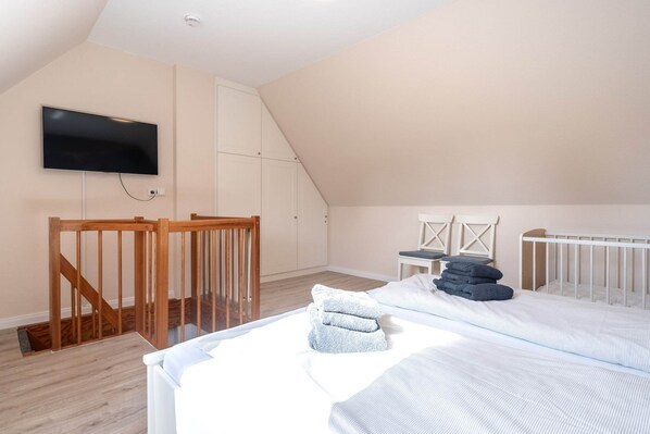 Une chambre avec un plafond en pente, un téléviseur fixé au mur, un berceau et un lit avec des serviettes.