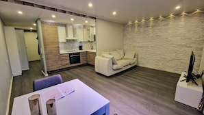 A modern living room with a sofa, a dining table with papers, and a kitchen area with a stone wall.