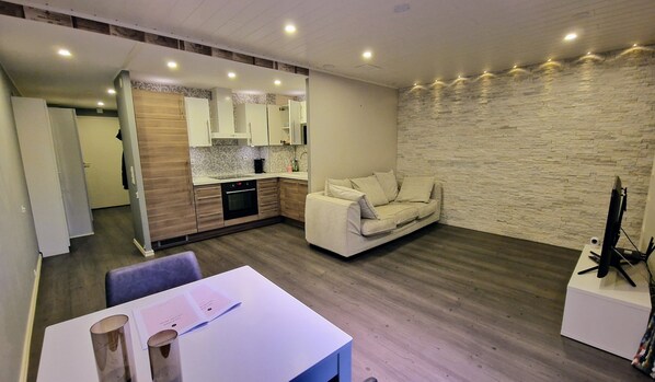 A modern living room with a sofa, a dining table with papers, and a kitchen area with a stone wall.