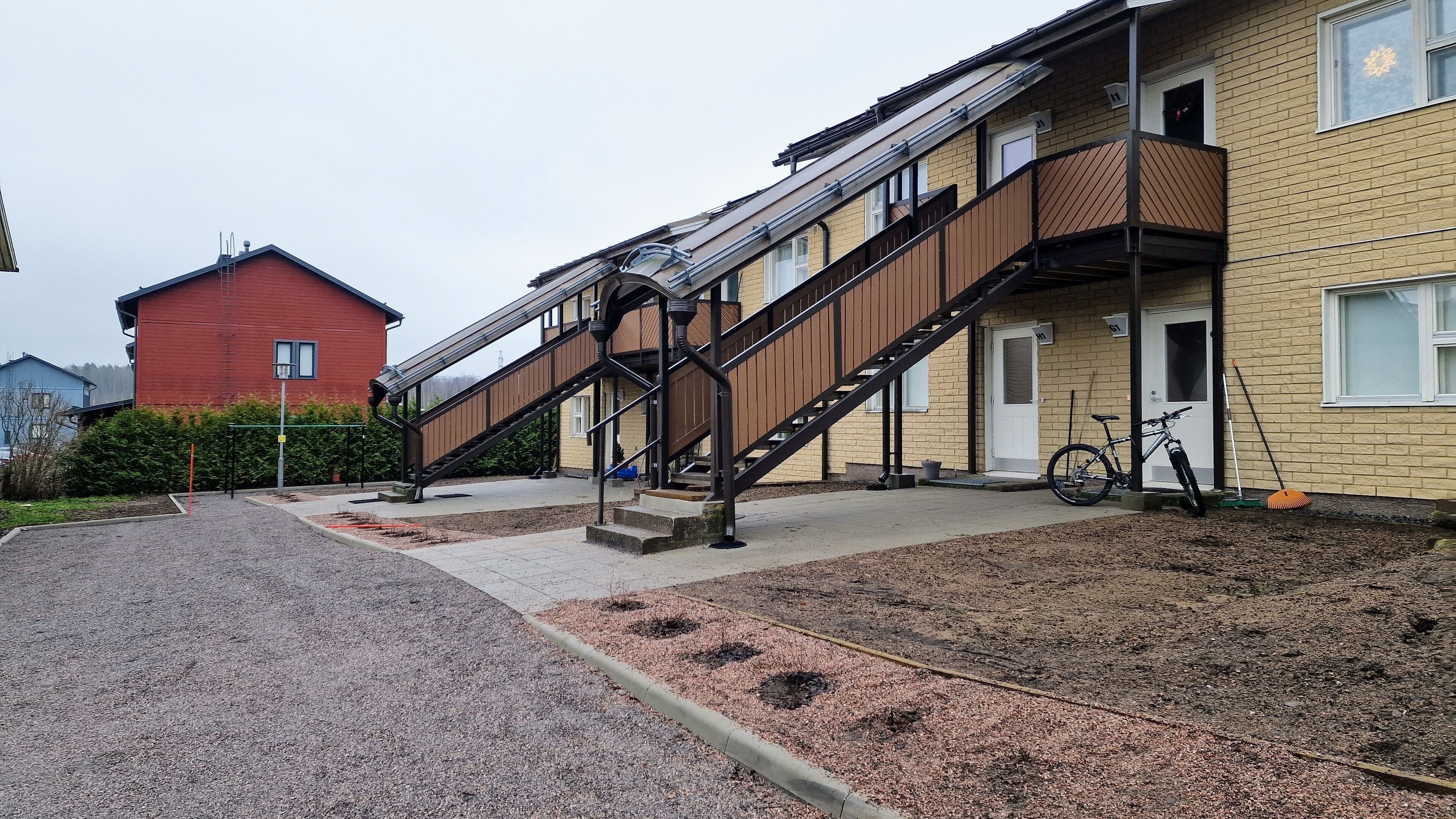 Un edificio residencial de varios pisos con una escalera, una bicicleta y una escoba apoyada en la pared.