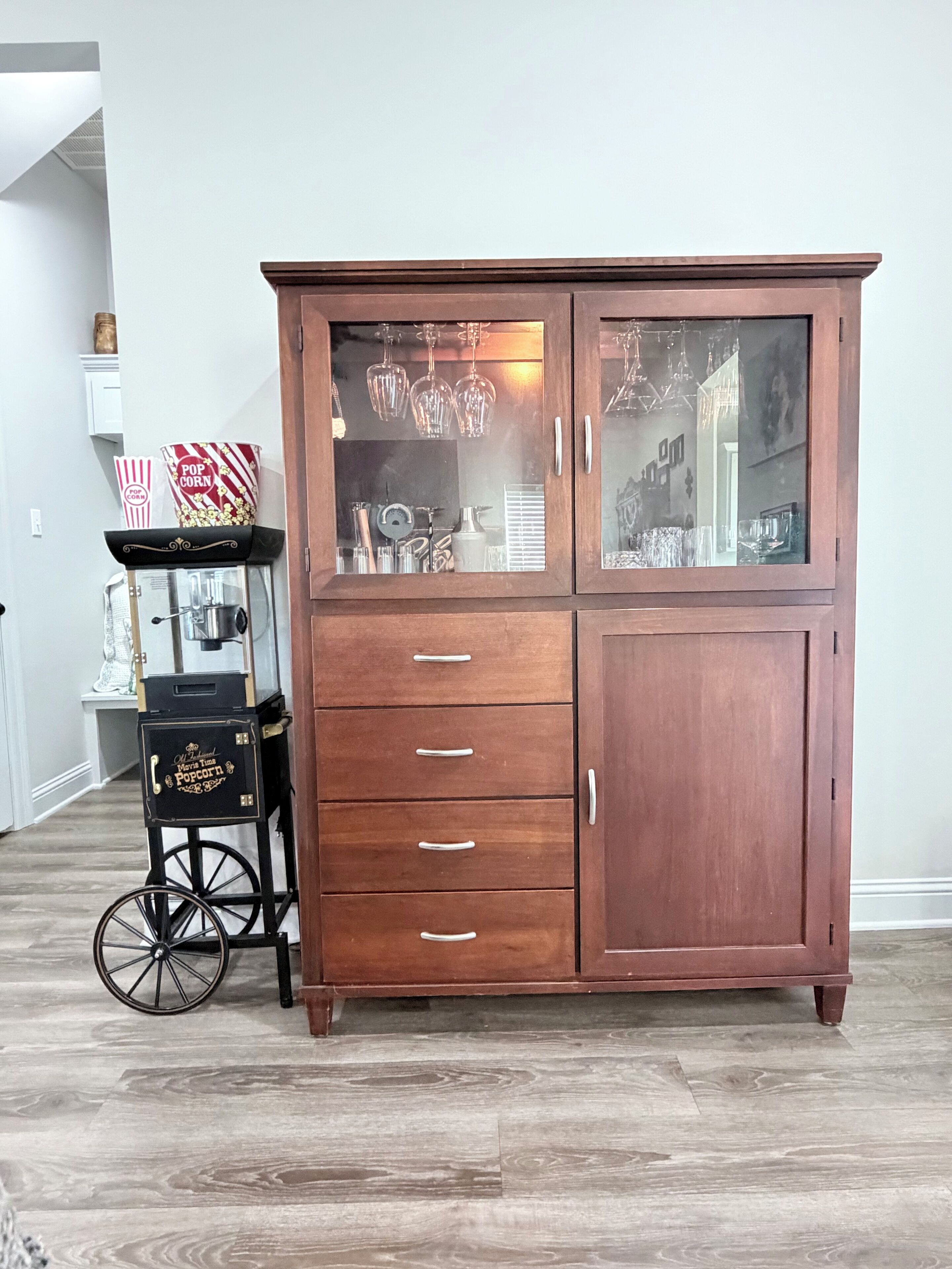 Un mueble de madera con puertas de cristal, un carrito de palomitas y una balanza antigua.