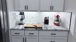 Una cocina con armarios blancos, encimera de granito, una licuadora, un juego de cuchillos y un robot de cocina rojo.