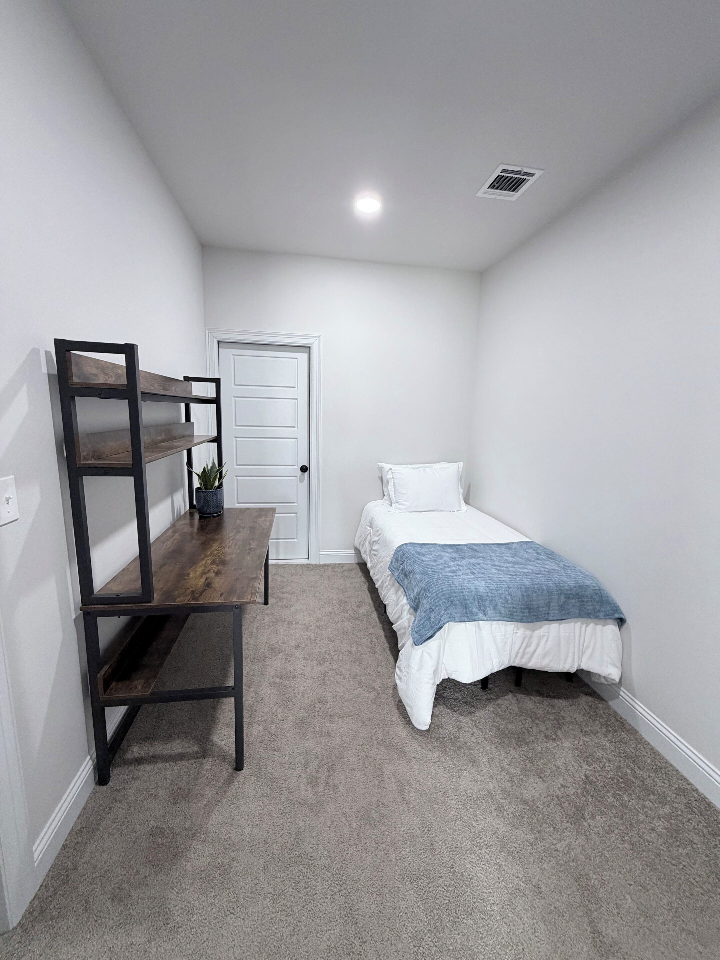 A bedroom with a bed, a desk, and a door.