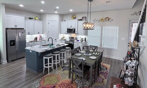 A modern kitchen with white cabinets, a stainless steel refrigerator, a built-in oven, and a large island with bar stools. - Wanderlust: Modern Home with Luxury Tub & King Bed 15m to Downtown (Shreveport)