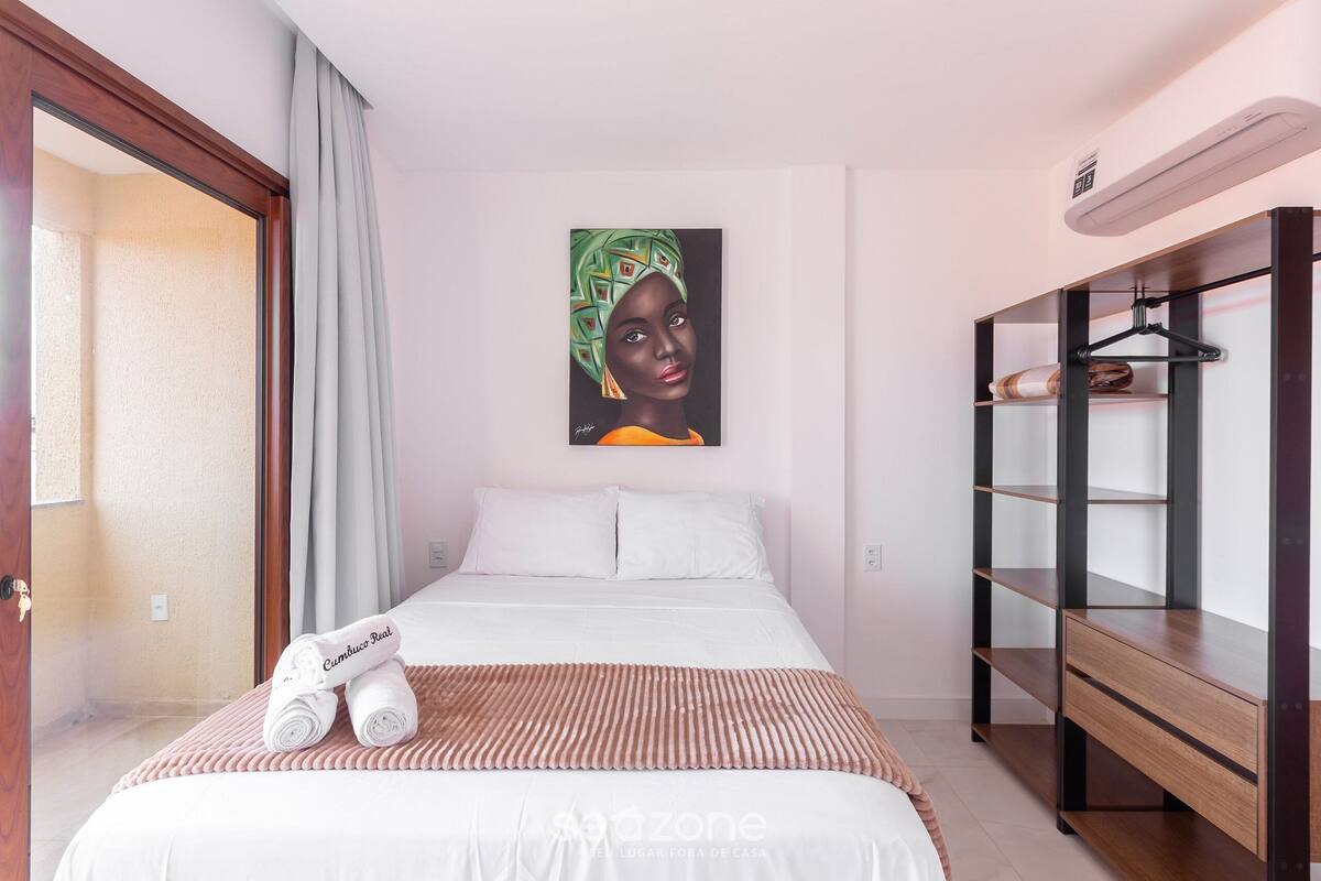 A hotel room with a bed, a painting, a wooden wardrobe, and a towel rack.
