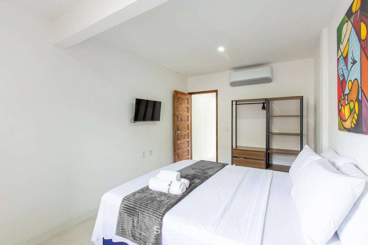 A hotel room with a bed, a TV, a wardrobe, and a painting on the wall.
