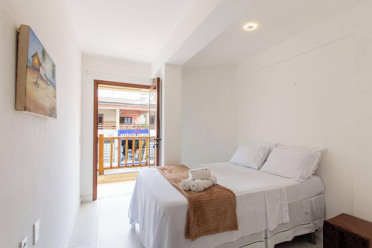 A bedroom with a bed, a bedside table, a window, and a view of a building outside.