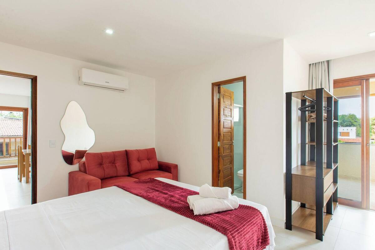 A hotel room with a bed, a red sofa, a mirror, and a sliding door leading to a balcony.