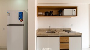 Une cuisine équipée d’un réfrigérateur, d’une machine à café, d’un four à micro-ondes et d’une étagère où sont rangés des verres.