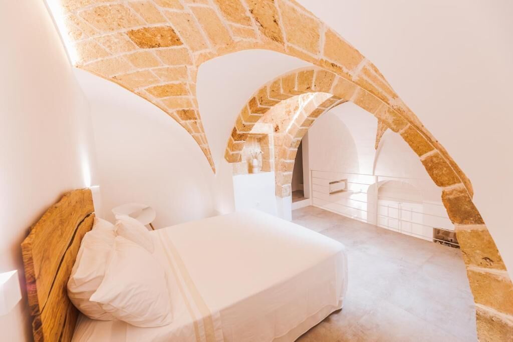 A bedroom with a white bed, a wooden headboard, and stone arches.