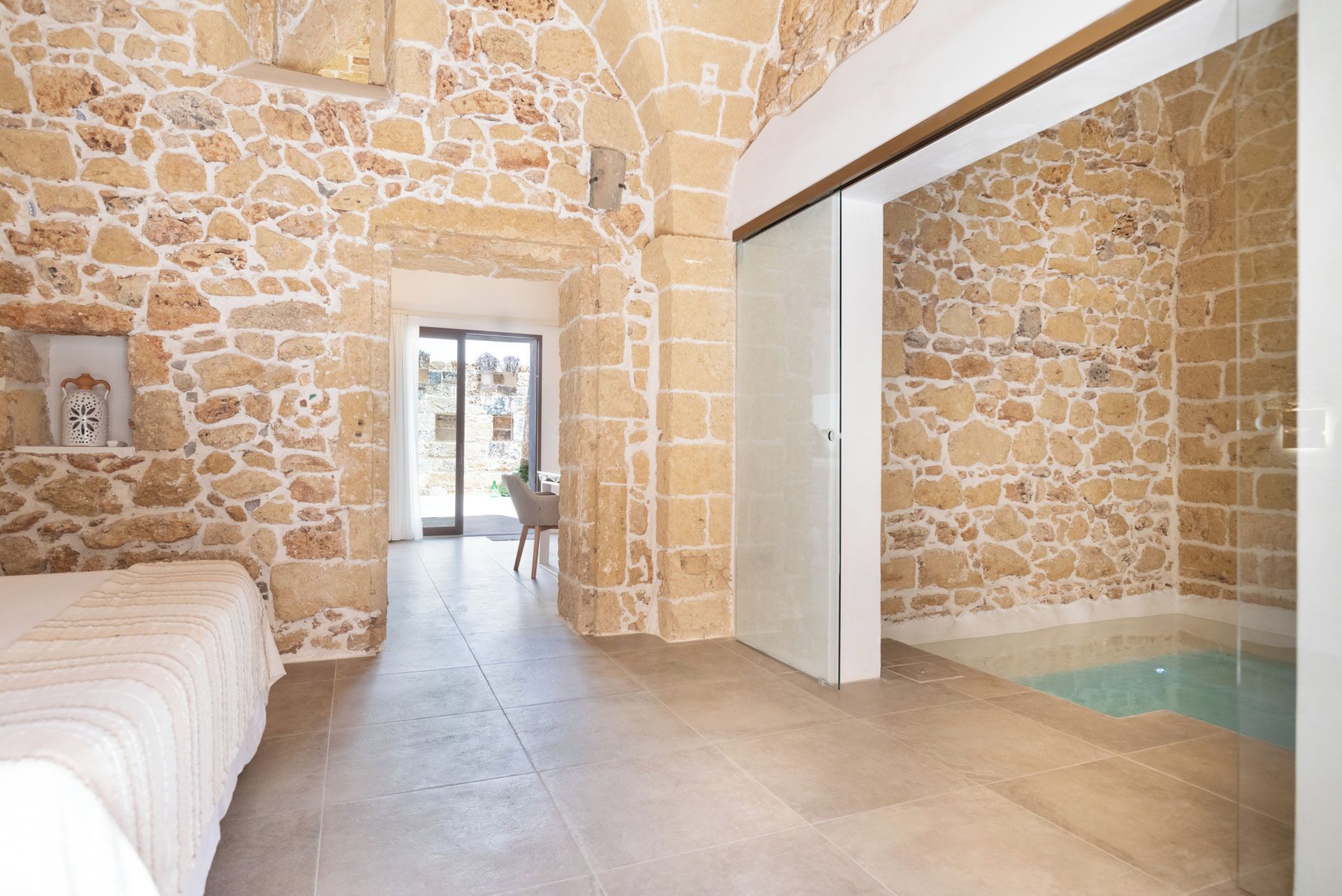 Camera con pareti in pietra, un letto, una sedia e un bagno con cabina doccia e vasca.