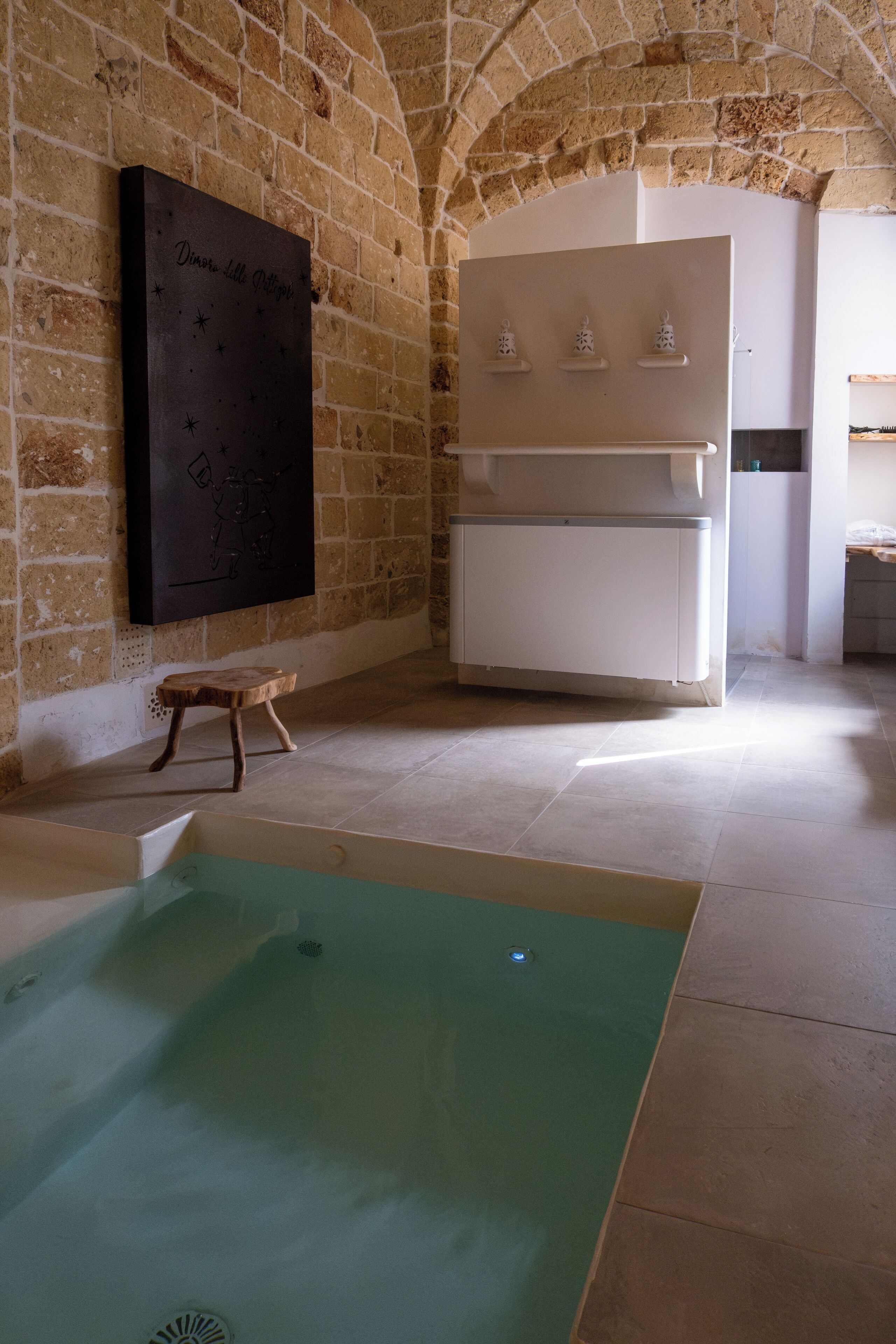 A spa area with a stone wall, a large painting, a wooden stool, a white cabinet, and a bathtub.